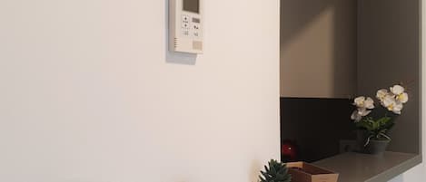 Un baño moderno con un estante empotrado que sostiene plantas en macetas y un termostato instalado en la pared.