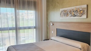 Un cuarto de hotel con cama, vista a través de cortinas translúcidas, un cuadro en la pared y una lámpara en el techo.