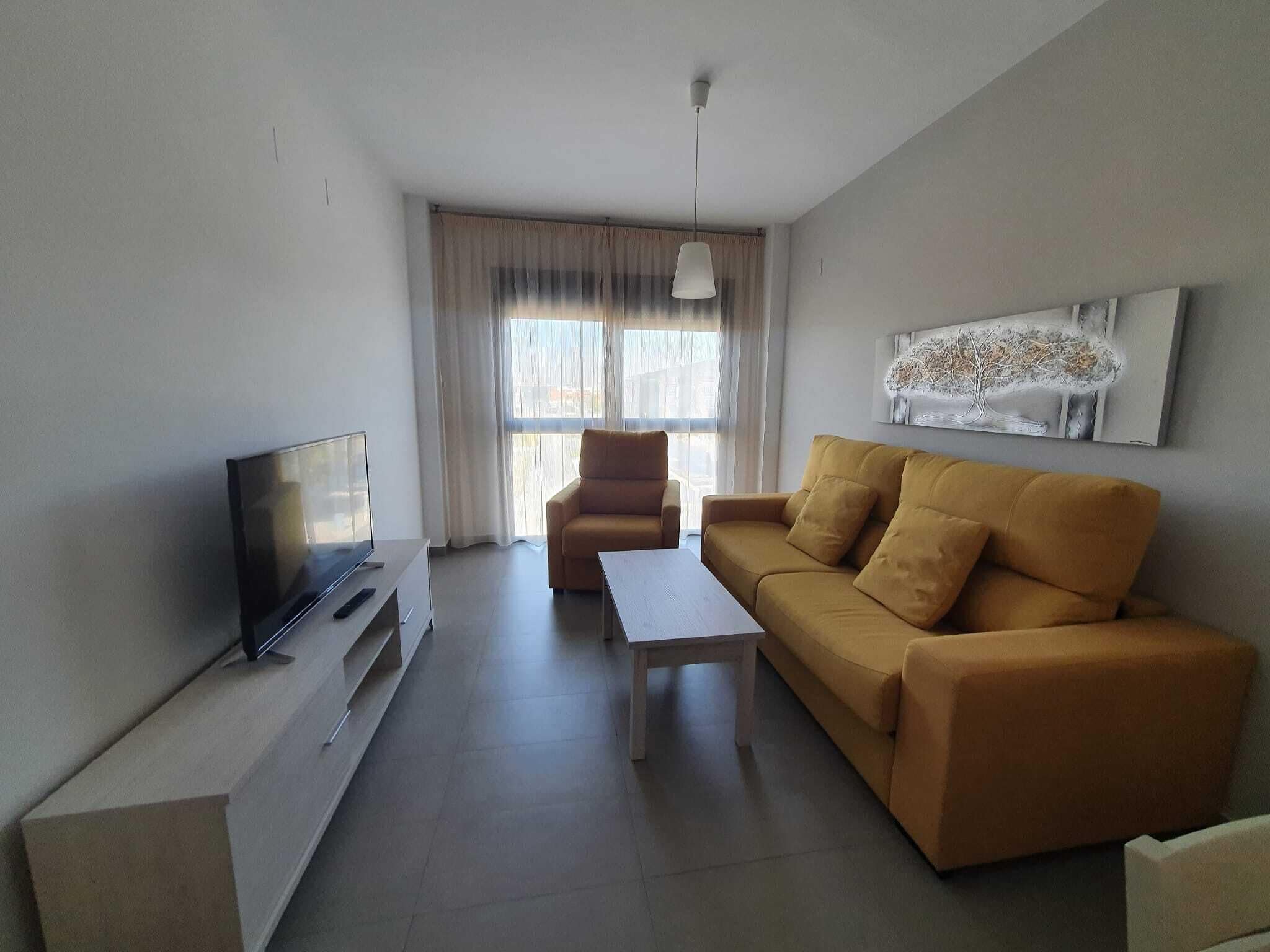 A modern living room with a flat-screen TV, a sofa, a coffee table, and a large window with curtains.