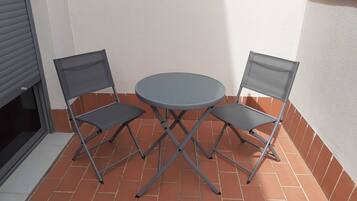 Een klein terras buiten met een ronde tafel en twee stoelen.