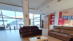 Amplia sala de estar con ventanas grandes, un sofá de cuero marrón, una mesa de centro blanca y una pared de acento roja.