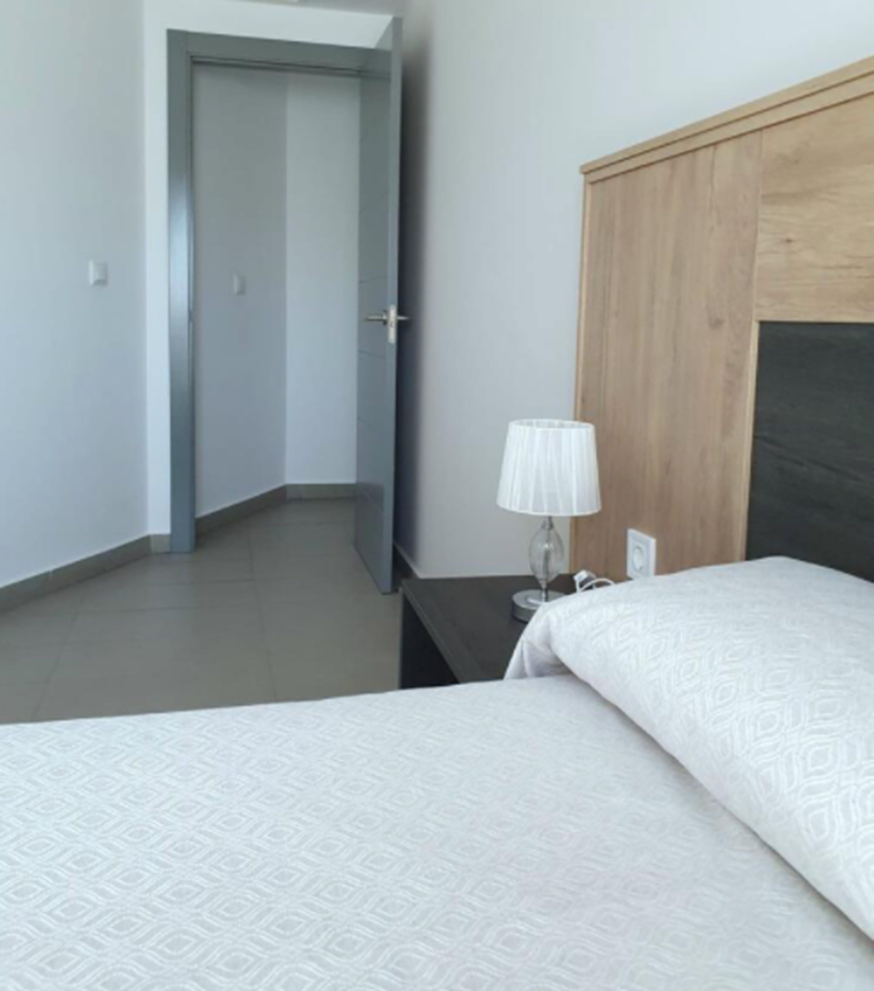 Habitación de hotel con cama, mesita de noche, lámpara y cabecero de madera.