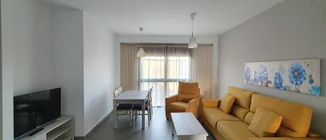 Een moderne woonkamer met een flatscreen televisie, een bank, een eettafel met stoelen en een schilderij aan de muur.