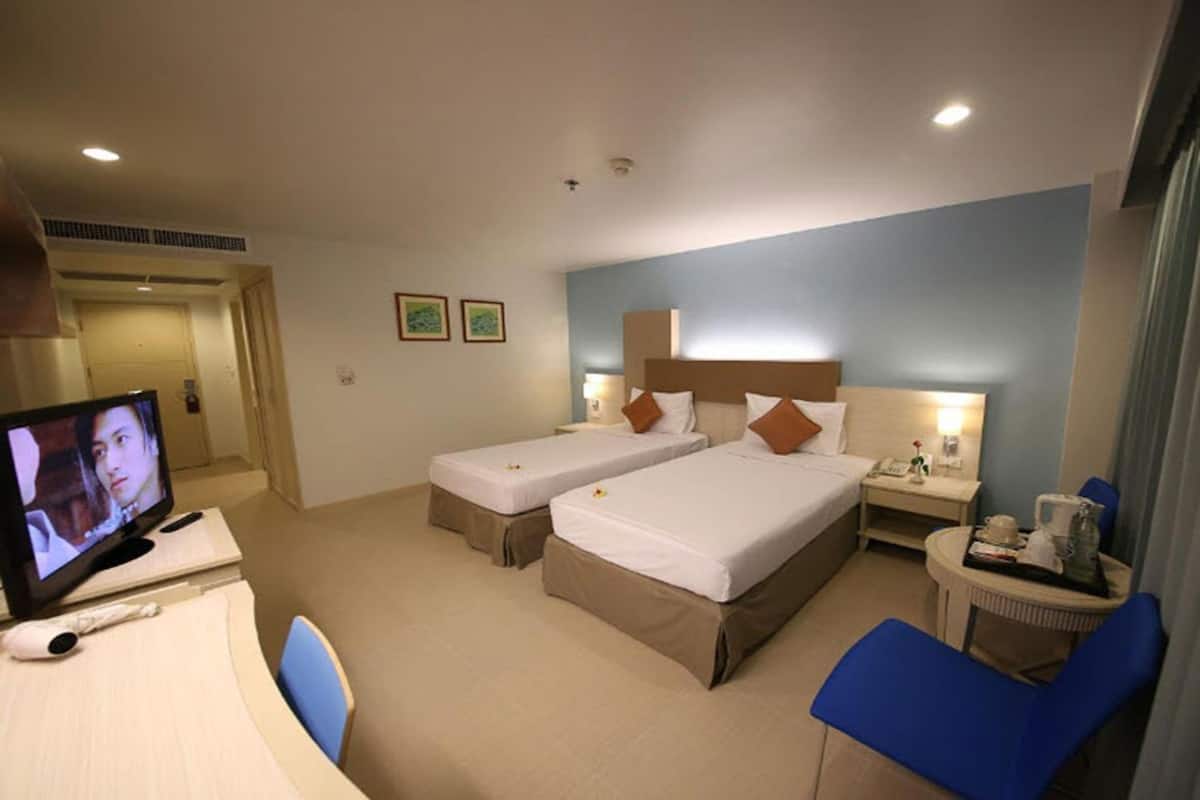 Ein Hotelzimmer mit zwei Betten, einem Fernseher, einem Schreibtisch mit Stuhl sowie einem Nachttisch mit Lampe.