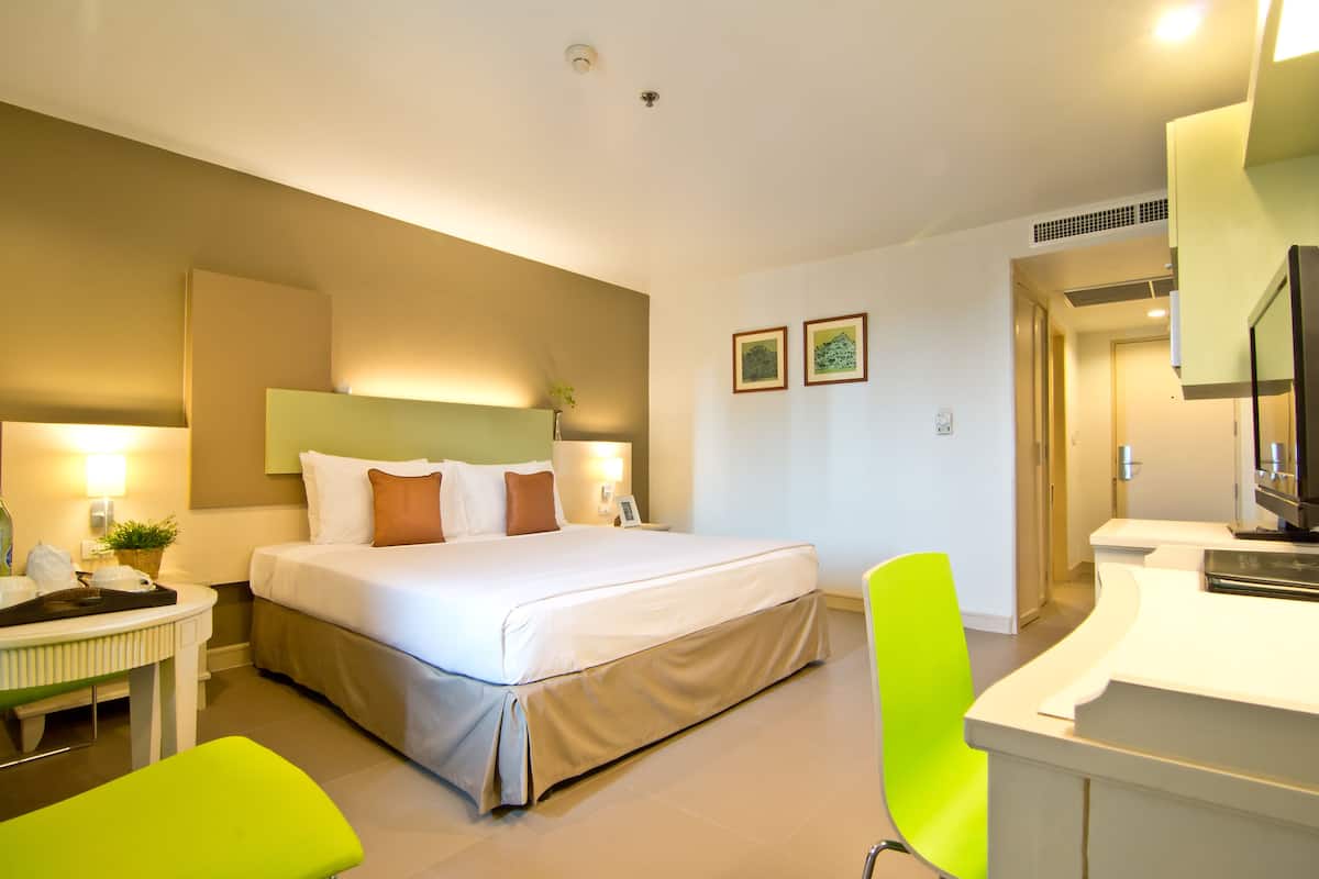 Ein modernes Hotelzimmer mit einem großen Bett, einem Schreibtisch, einem leuchtend grünen Sessel und einem durch eine offene Tür einsehbaren Badezimmer.