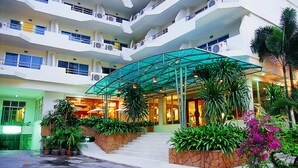 A multi-story hotel with a central atrium, outdoor seating area, and lush landscaping. - SUNSHINE VISTA (Pattaya)