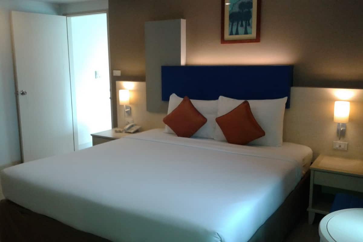 Ein Hotelzimmer mit einem großen Bett, zwei Nachttischen, einer Wandlampe und einer Tür.