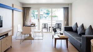 A modern living room with a sofa, coffee table, and chairs. There is a television on a stand, a dining table with chairs, and a large window with curtains. - SUNSHINE VISTA (Pattaya)