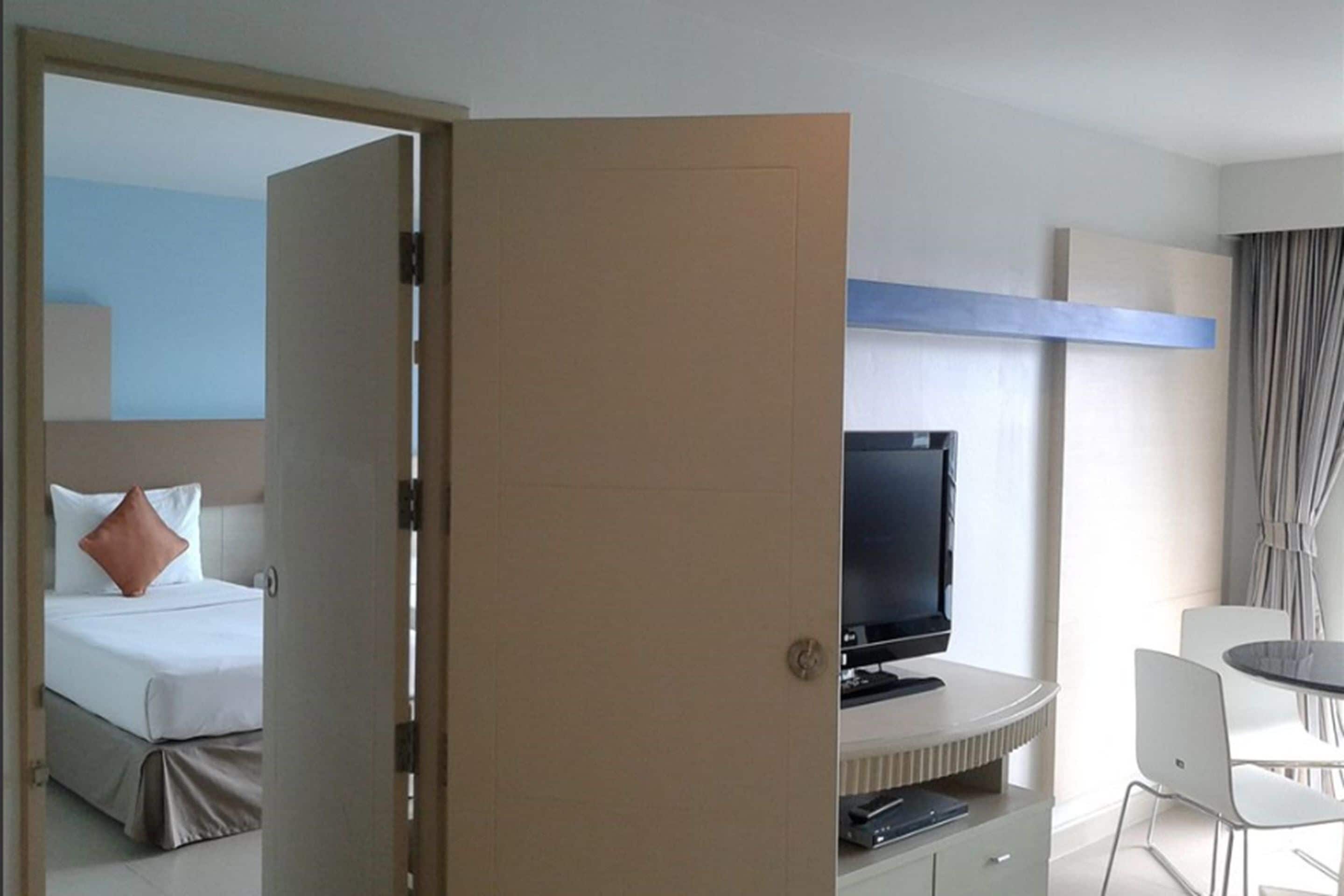 A hotel room with a bed, a TV, a desk with a chair, and a dining area.