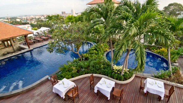 A poolside area with tables and chairs, surrounded by lush greenery and palm trees. - SUNSHINE VISTA (Pattaya)