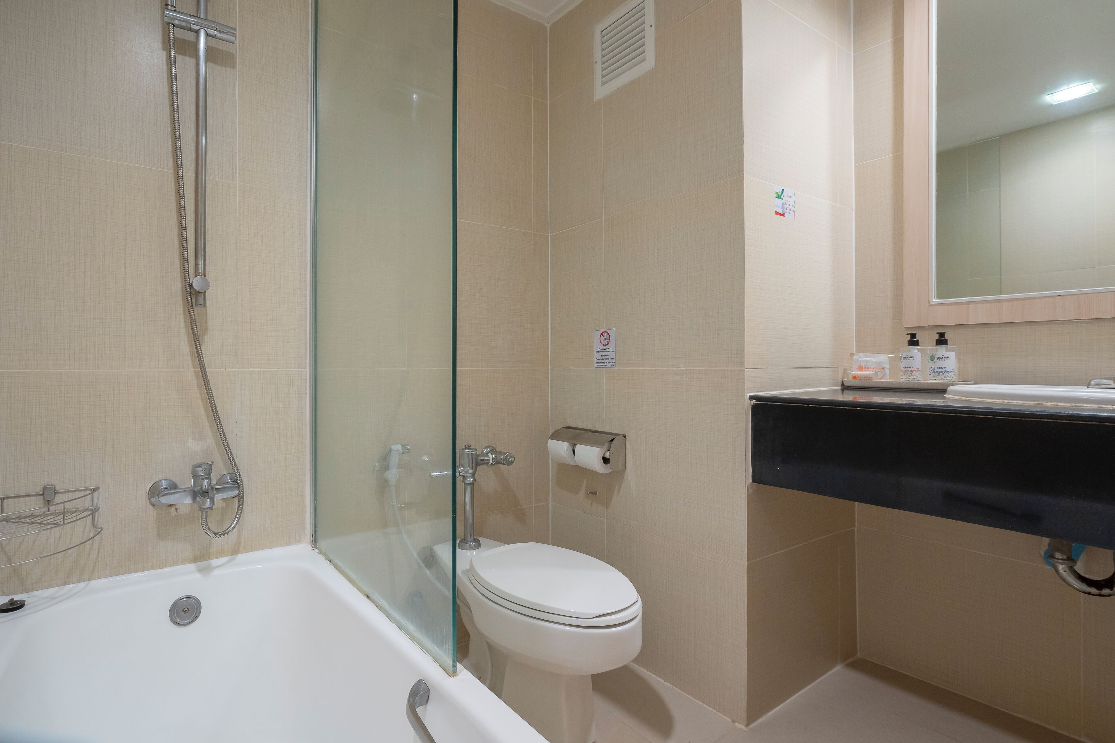 A bathroom with a glass-enclosed shower, a toilet, and a sink with soap dispensers.