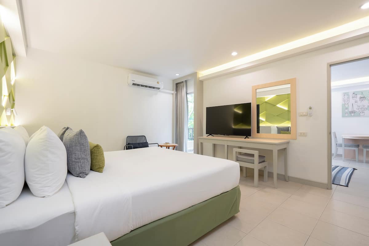 A hotel room with a large bed, a desk with a flat-screen TV, a chair, and a dining area with a table and chairs.