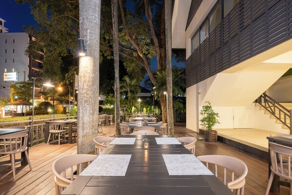 An outdoor dining area with tables and chairs, surrounded by trees and buildings.