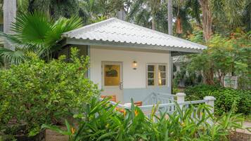 Una casita de techo blanco, rodeada de exuberante vegetación y palmeras.