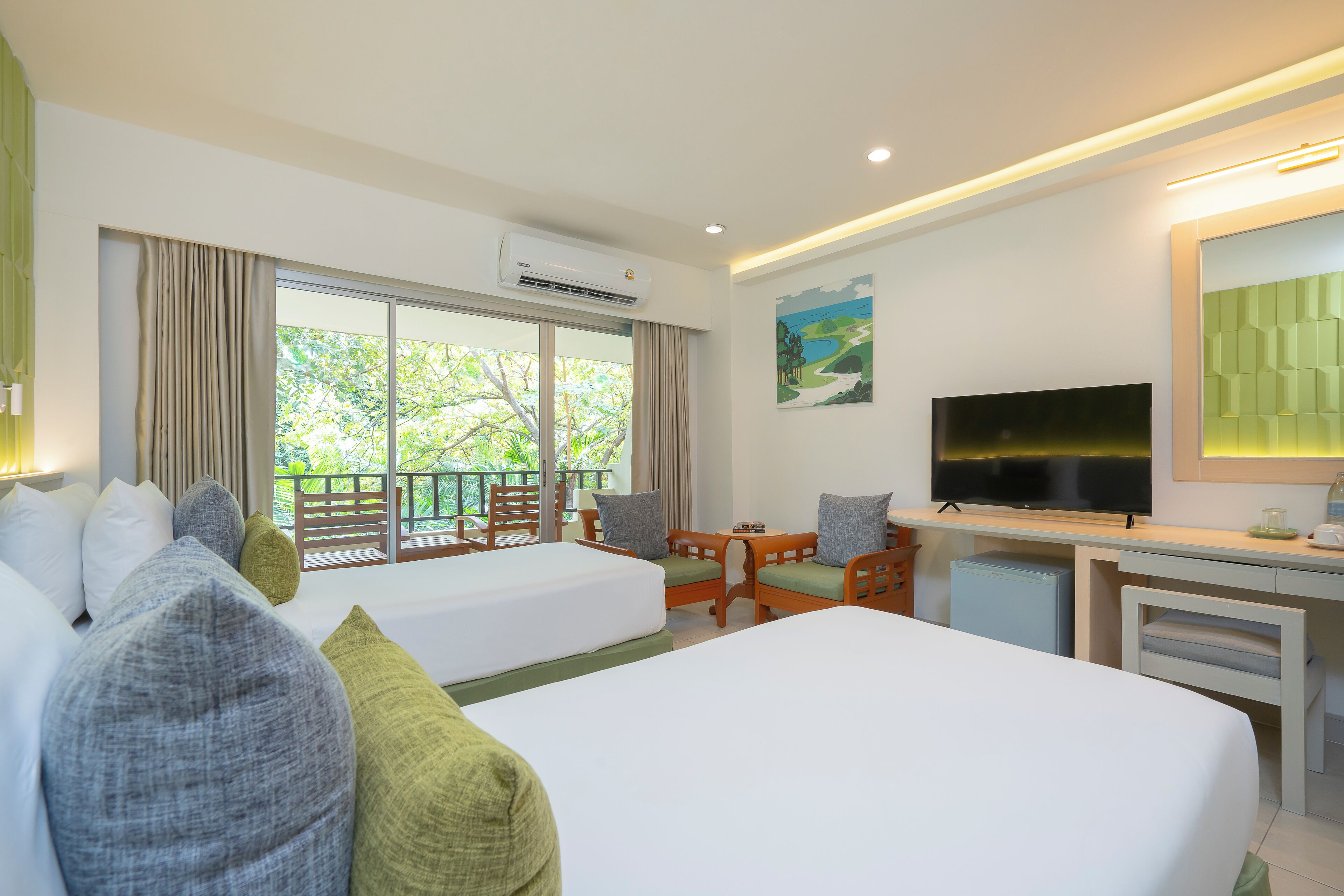 A hotel room with two beds, a desk, a TV, and a balcony with a view of trees.