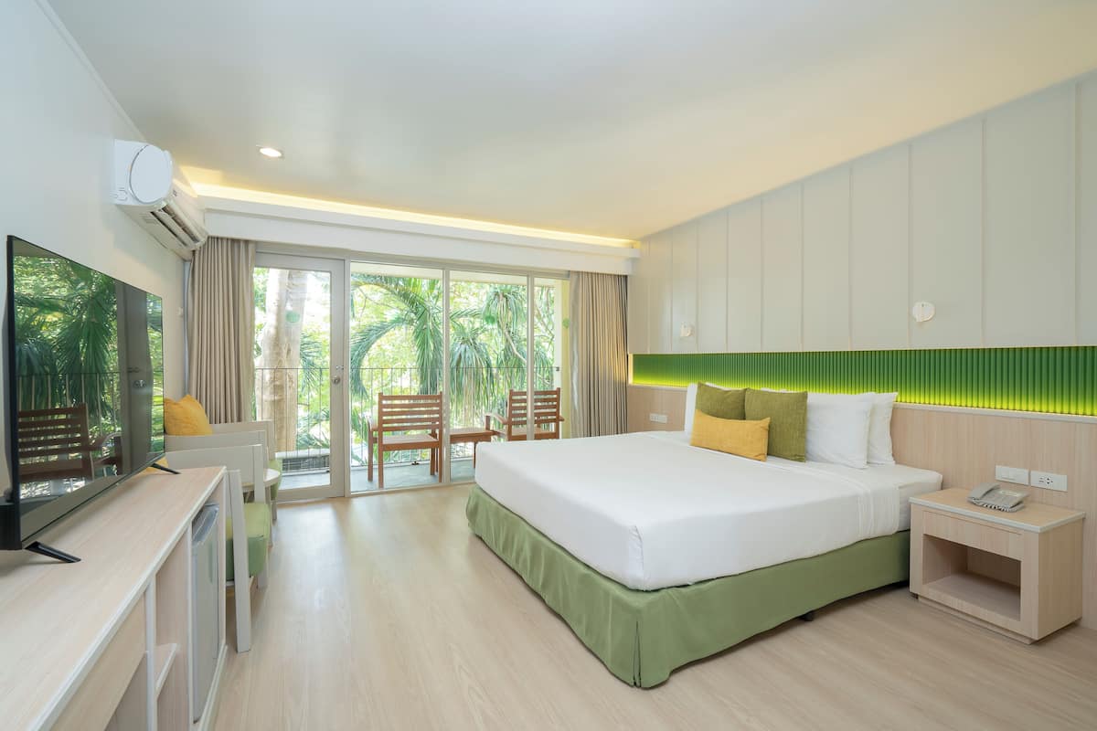 A modern hotel room with a large bed, a desk with a flat-screen TV, a small bedside table with a phone, and a balcony with a view of palm trees.
