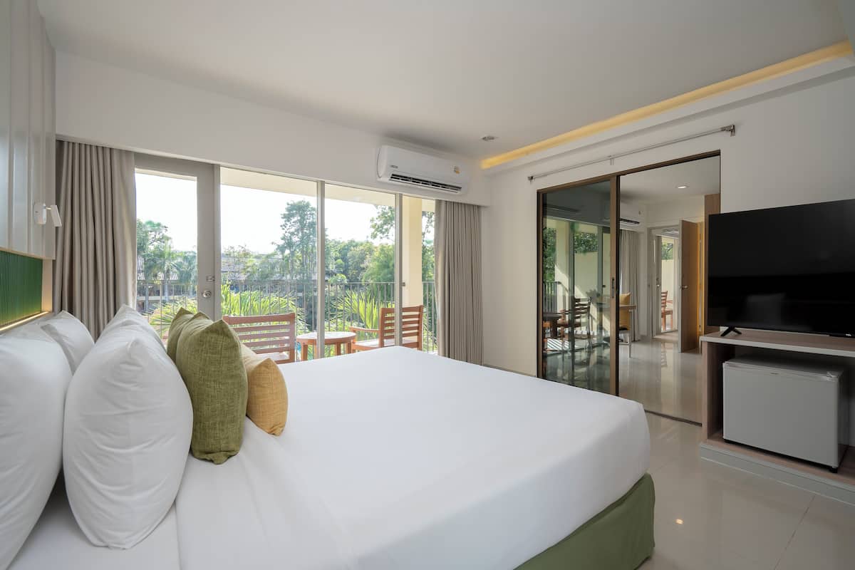 A hotel room with a large bed, a flat-screen TV, a mini-fridge, and a balcony with outdoor seating.