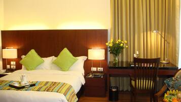 Habitación de hotel con cama, lámparas de noche, escritorio con silla, un jarrón con flores y frutero.