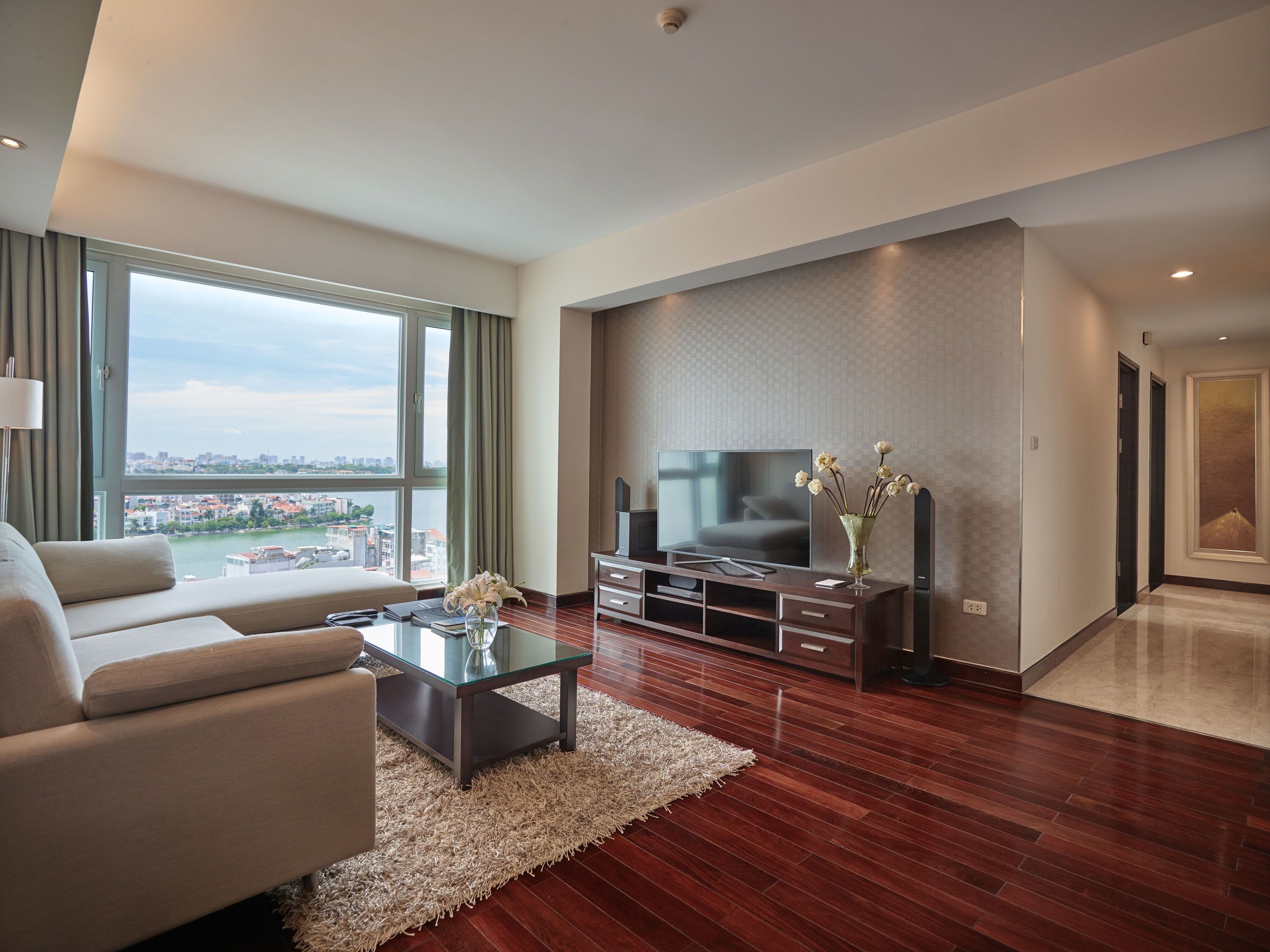 Una sala de estar moderna con un televisor grande, asientos cómodos, una mesa de centro de vidrio y vistas de la ciudad.