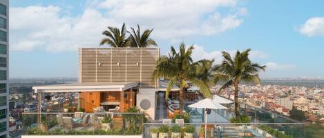 A rooftop bar with outdoor seating, palm trees, and a city view.