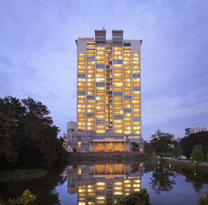 Un hotel de gran altura con varios pisos, una piscina reflectante al frente y el nombre 'FRASERS SUITES' visible en el edificio.