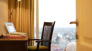 A room with a view of a cityscape through a window, a wooden chair, a desk with a laptop and a book titled "The New History of Photography."