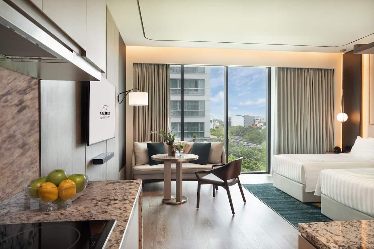 A hotel room with a sofa, a dining table, a bed, and a view of the city.