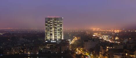 Un hotel moderno de gran altura con un letrero llamativo, ubicado junto a la costa con luces de la ciudad al fondo.