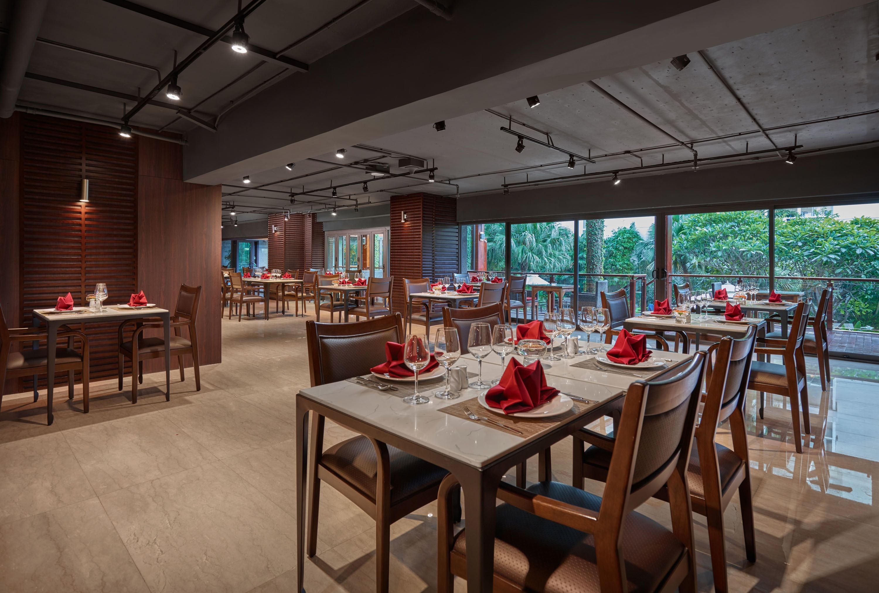 Een restaurant met meerdere tafels gedekt voor diners, grote ramen met uitzicht op groen, en een modern interieur.
