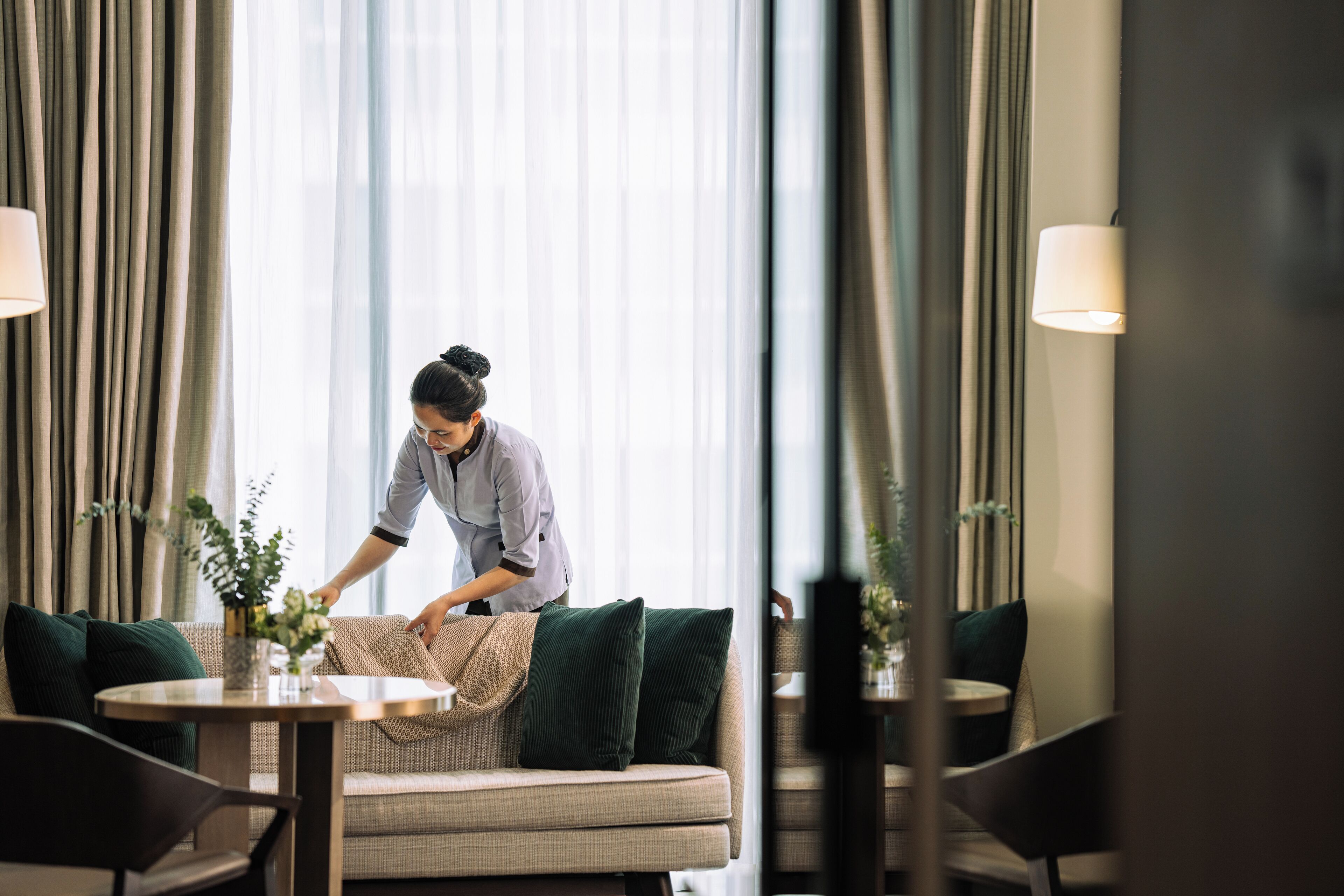Een hotelkamer met een bank, een bijzettafeltje met een bloemenvaas, en een lamp.
