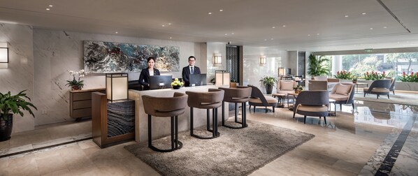 Un moderno vestíbulo de hotel con mostrador de recepción, taburetes de bar, zona de estar y ventanas amplias que ofrecen vistas al exterior.