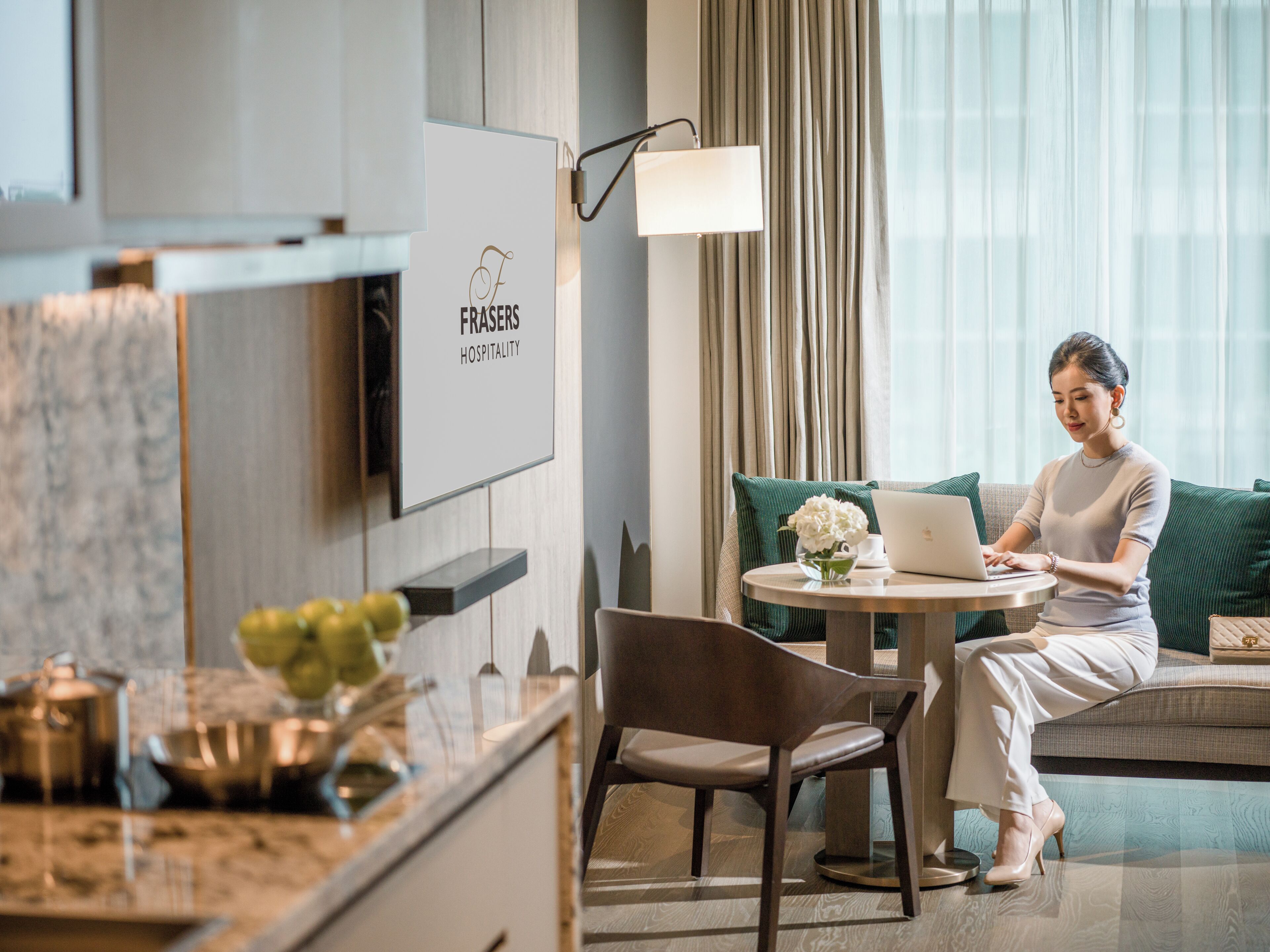 A modern hotel room with a dining area, a sofa, and a laptop on a table.