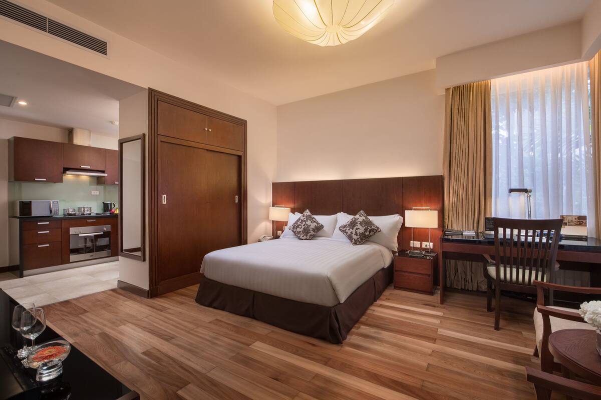 A hotel room with a bed, desk, chair, and kitchenette.