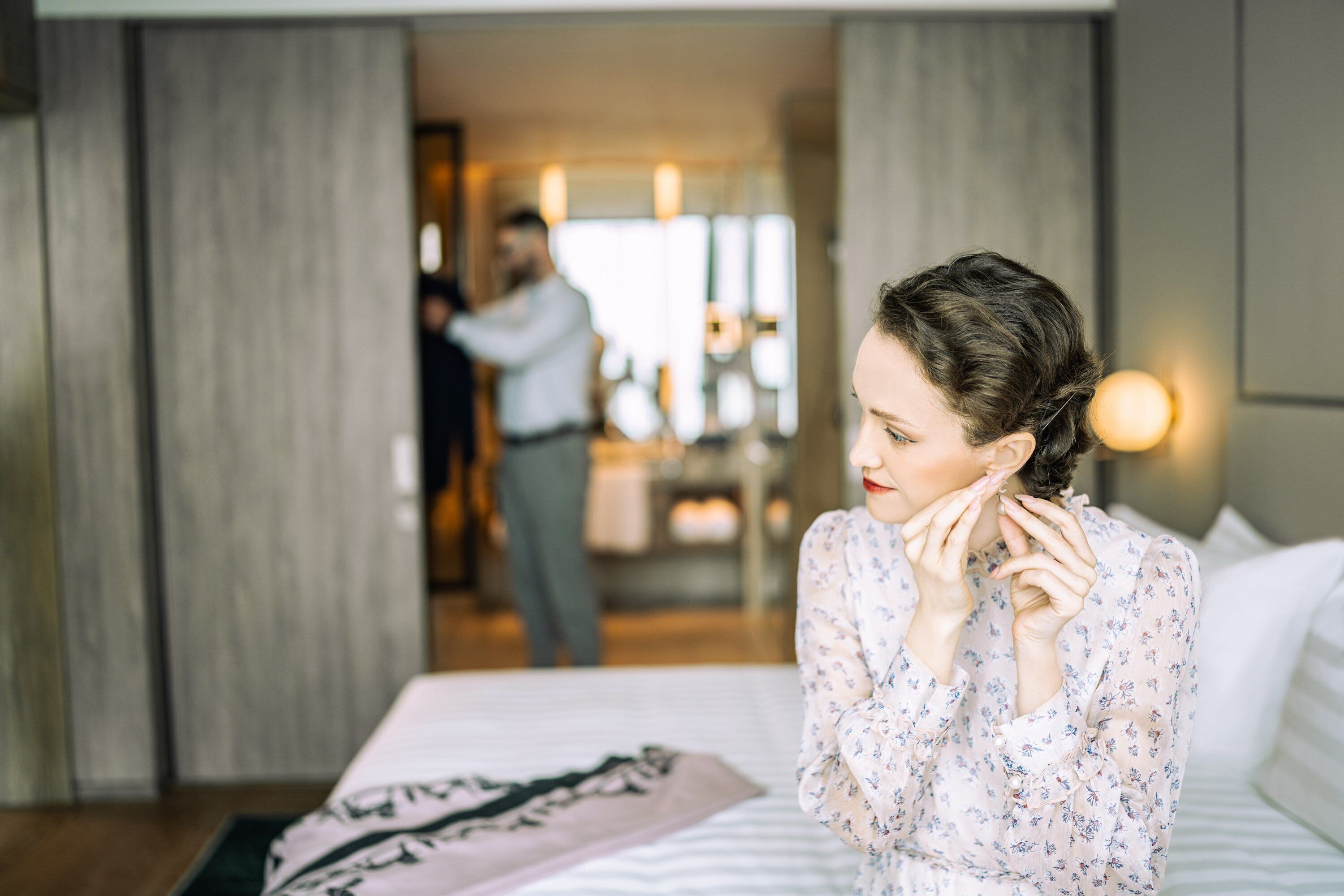 Habitación de hotel con cama, mesita de noche y espejo. Se ve a una persona en el fondo, cerca de la puerta.