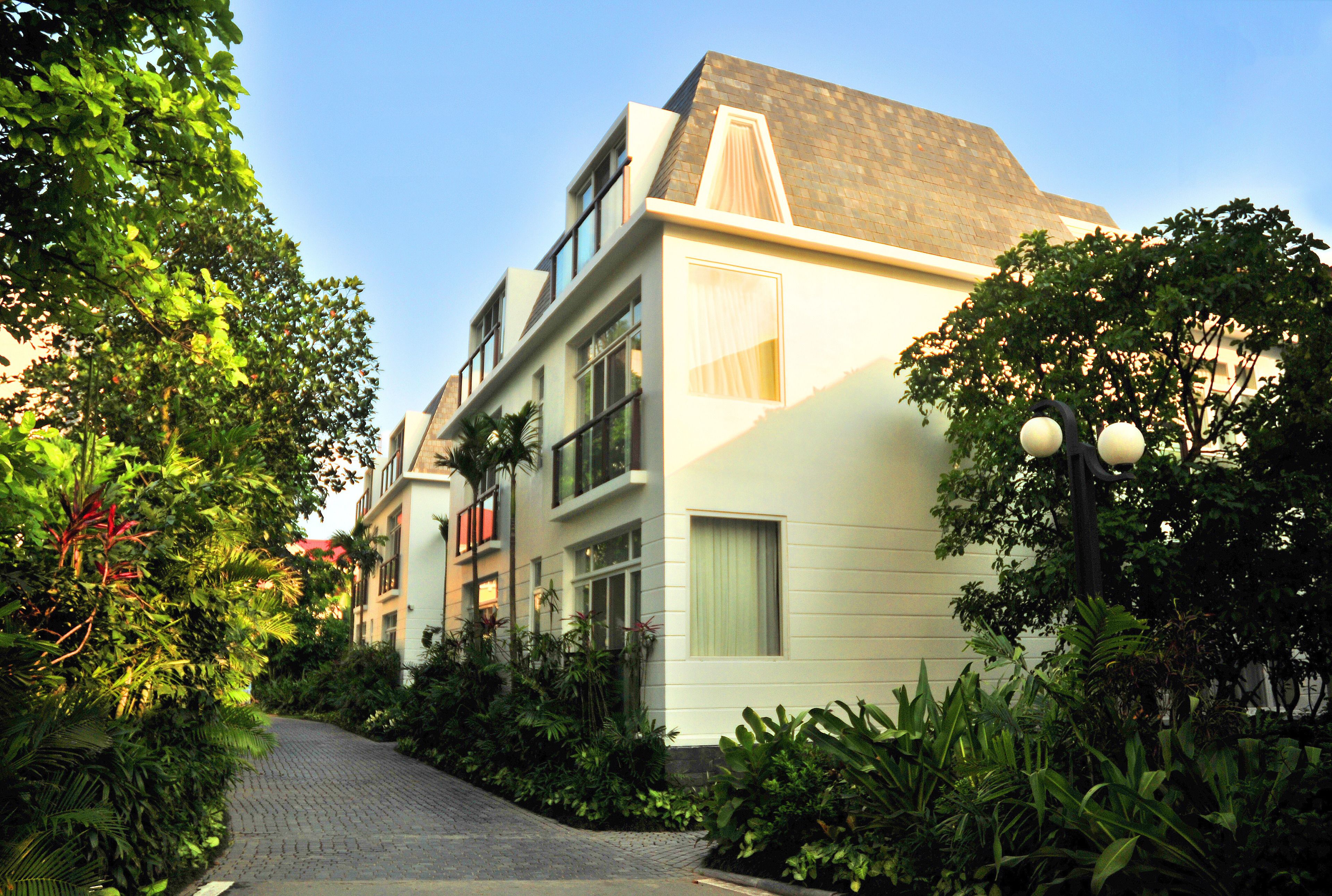 A modern building with a brick roof, large windows, and a pathway surrounded by lush greenery.