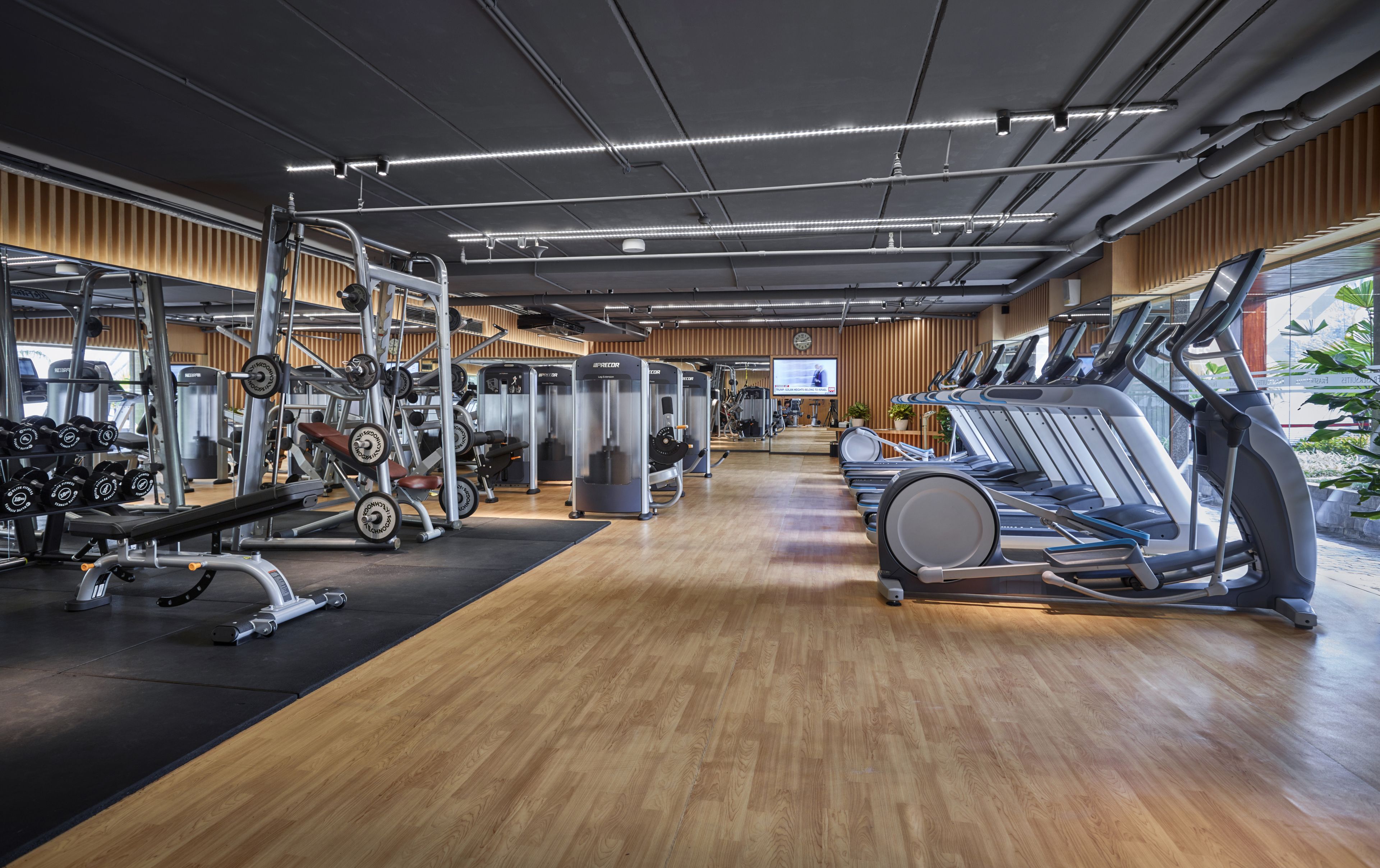 Een moderne sportschool met diverse fitnessapparaten, houten vloeren en grote ramen.