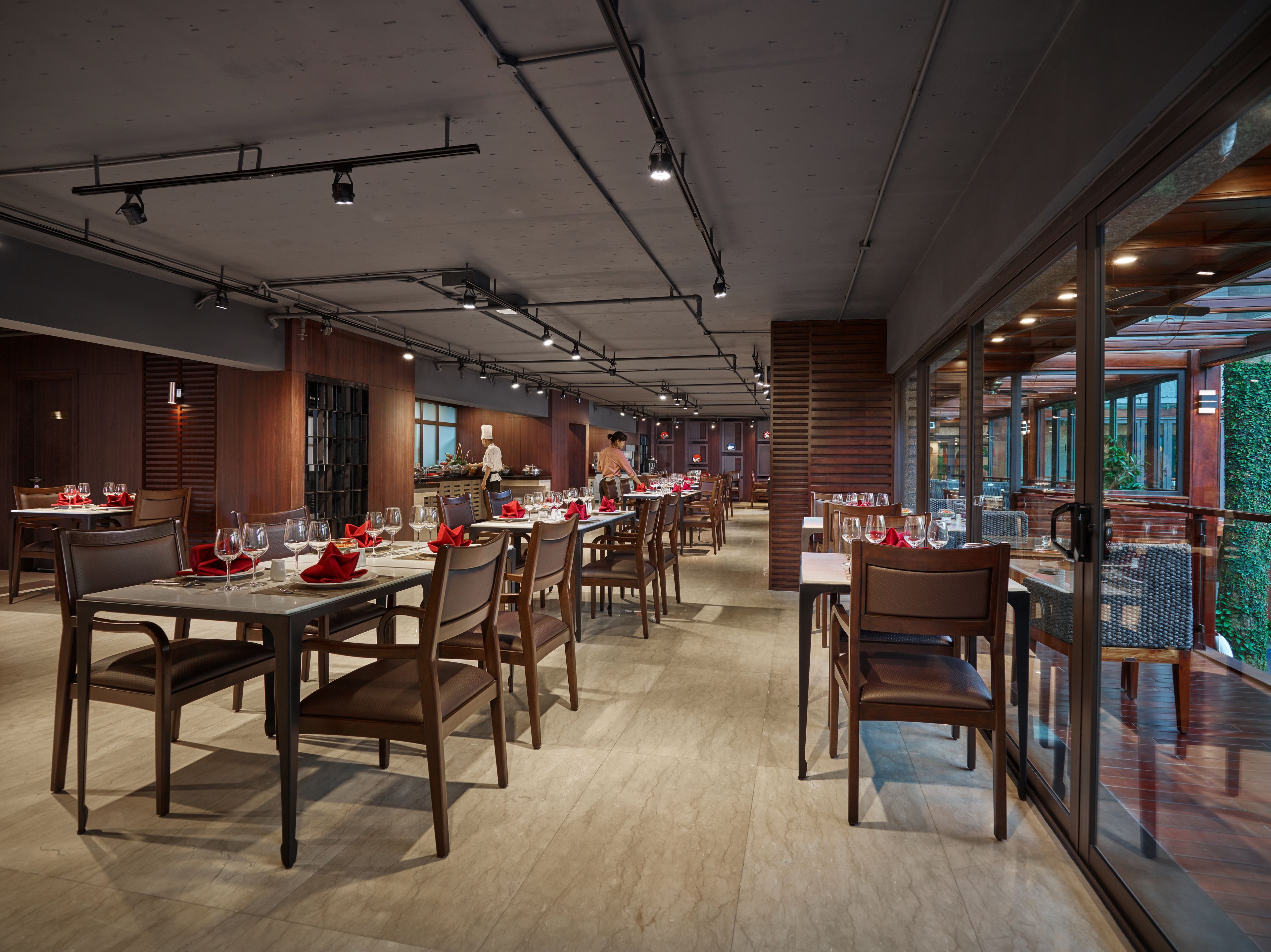 Ein Restaurant mit Holztischen und -stühlen, einer Küche im Hintergrund und großen Fenstern.
