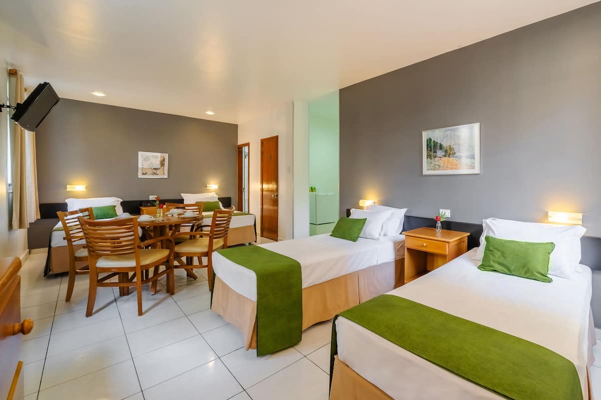Une chambre d’hôtel avec deux lits, un coin repas et un téléviseur fixé au mur.