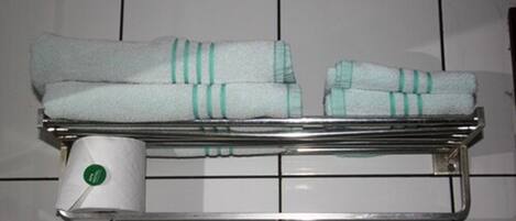 A metal towel rack with folded towels and a roll of toilet paper.