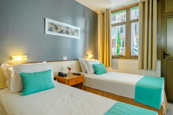 Ein Hotelzimmer mit zwei Betten, einem Nachttisch, einem gerahmten Bild an der Wand und einem Fenster mit Vorhängen.