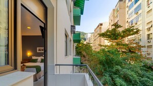 A residential building with a balcony, a view of a garden, and a bedroom with a bed and a nightstand.