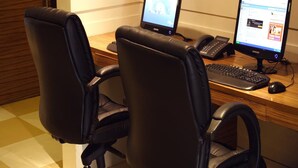 Um espaço de trabalho com duas cadeiras de escritório pretas, uma mesa de madeira, dois monitores Samsung, um teclado, um rato e um telefone.