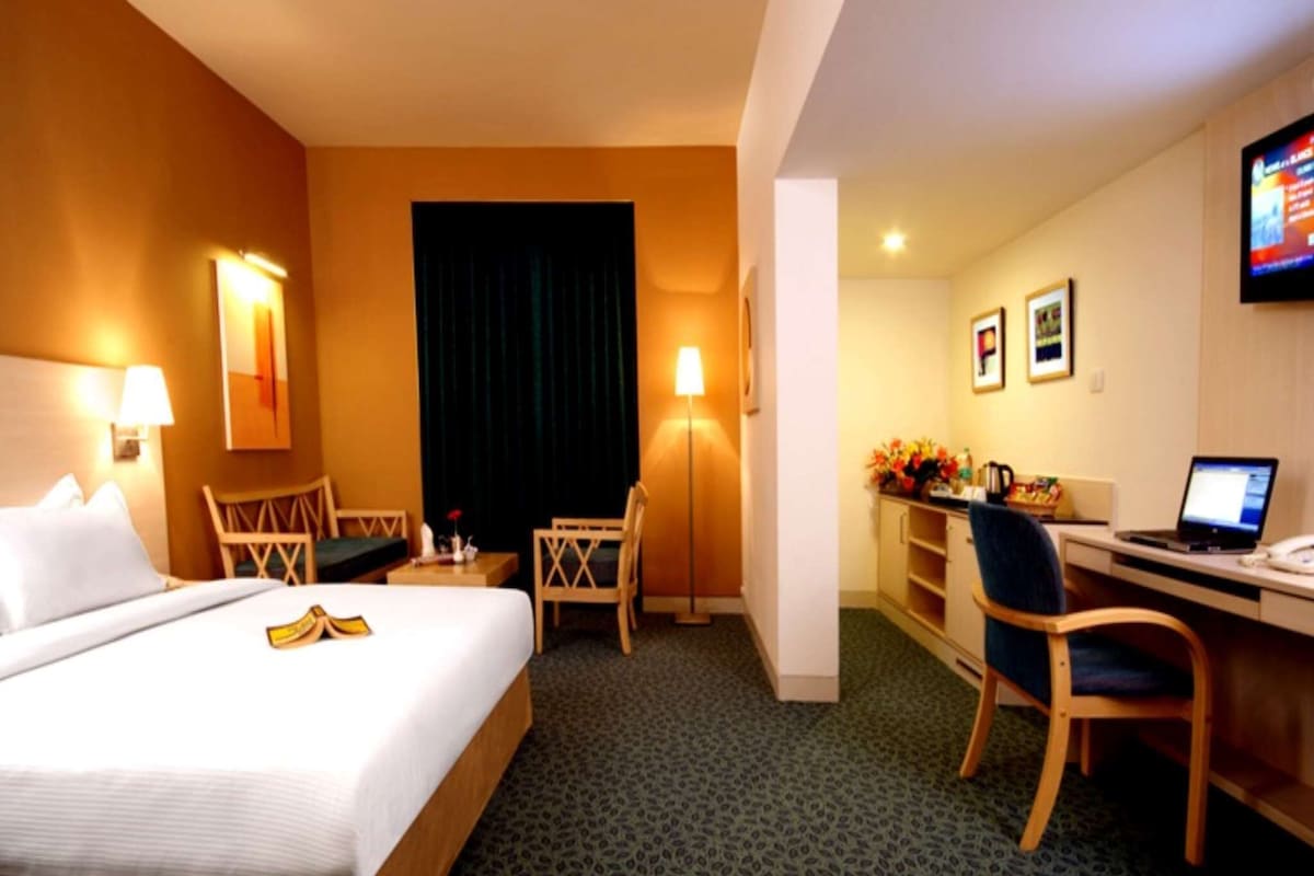 A hotel room with a bed, desk, chair, and a television on the wall.