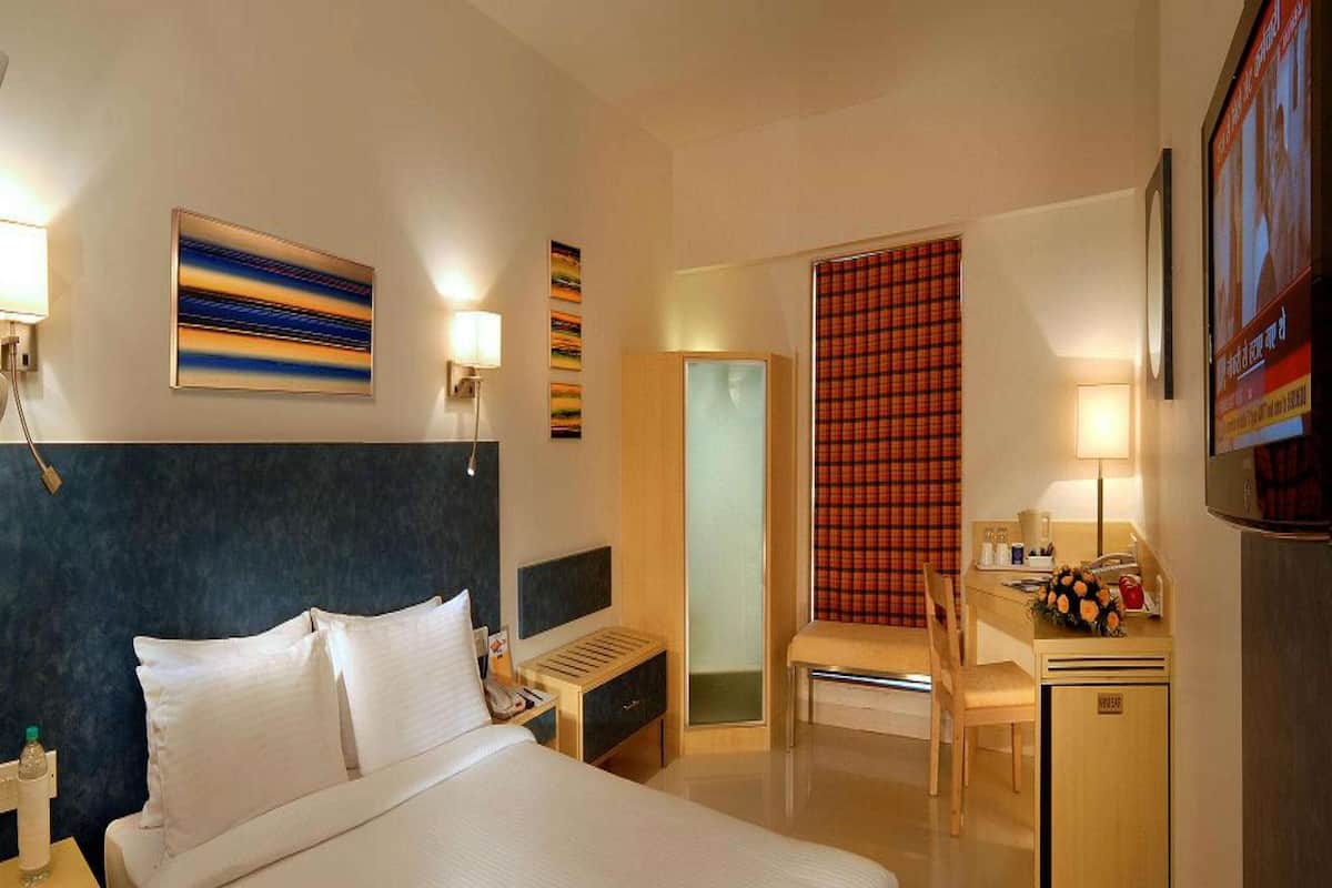 Een hotelkamer met een groot bed, een bureau met stoel, een kleine koelkast, een bureaulamp, een telefoon en een schilderij aan de muur.