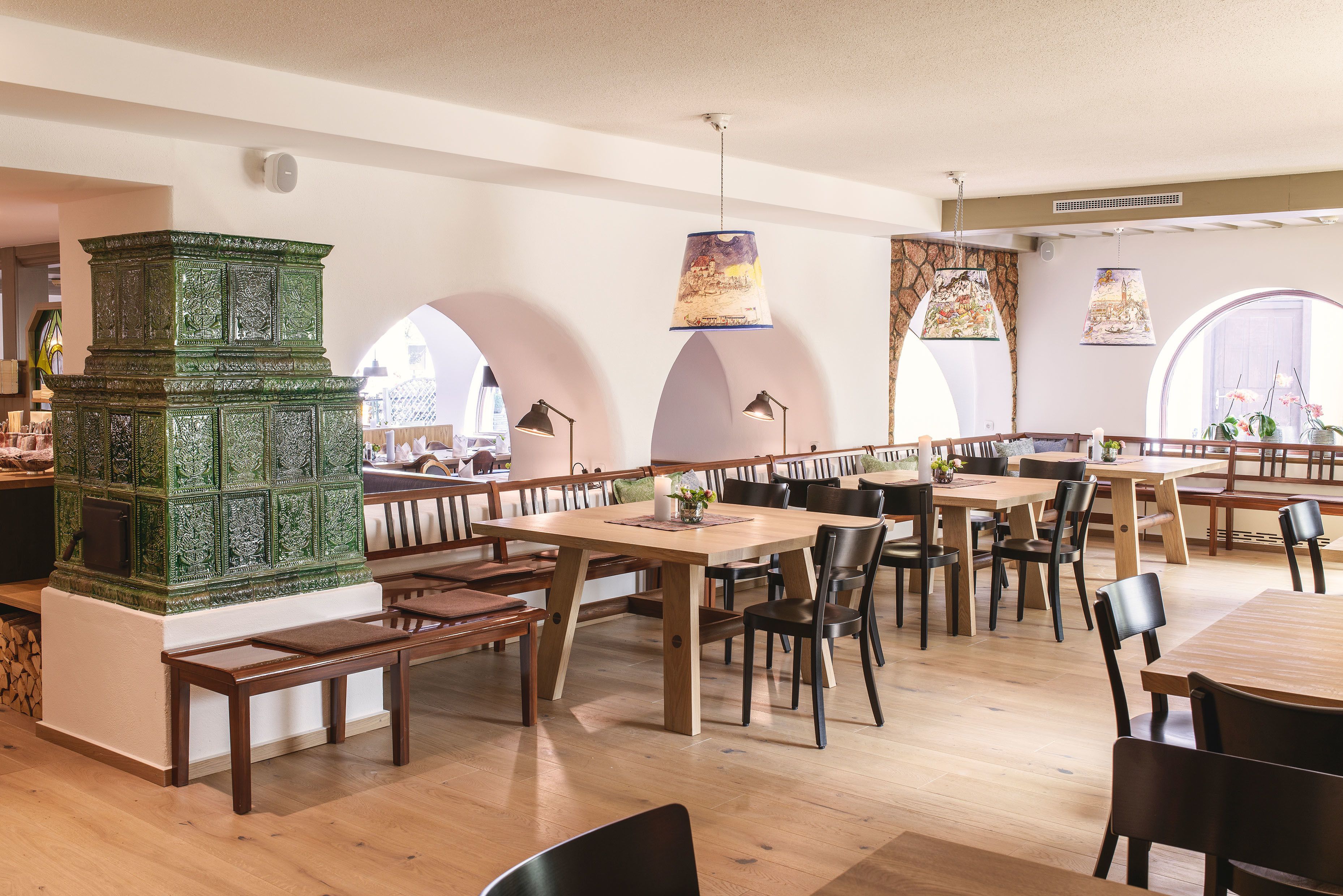 A spacious restaurant with wooden tables and benches, a green decorative piece, and arched windows.