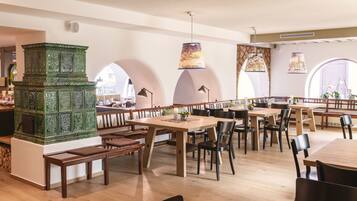 A spacious restaurant with wooden tables and benches, a green decorative piece, and arched windows.