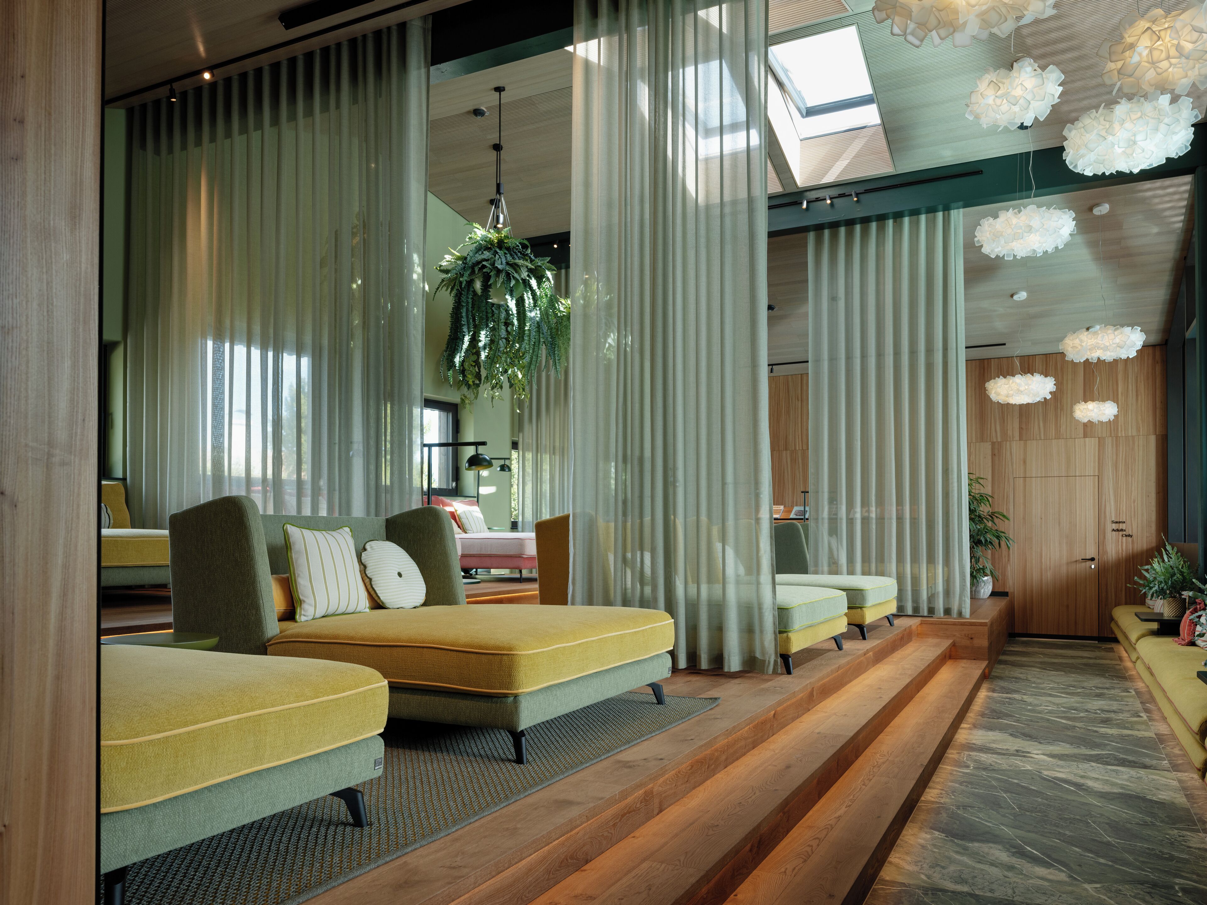A modern hotel lobby with a long reception desk, a seating area with sofas and chairs, and a large window with sheer curtains.