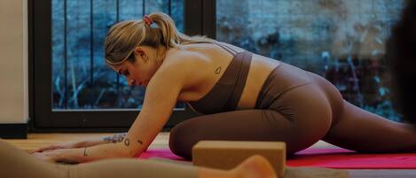 Una persona realizando una postura de yoga sobre una colchoneta roja en una habitación con un ventanal grande y suelo de madera.