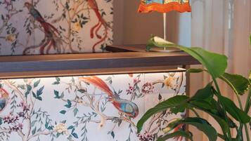 Een kamer met een houten plafond, een muur met behangpapier met vogelmotieven, een tafel met een vogelbeeldje en een plant.