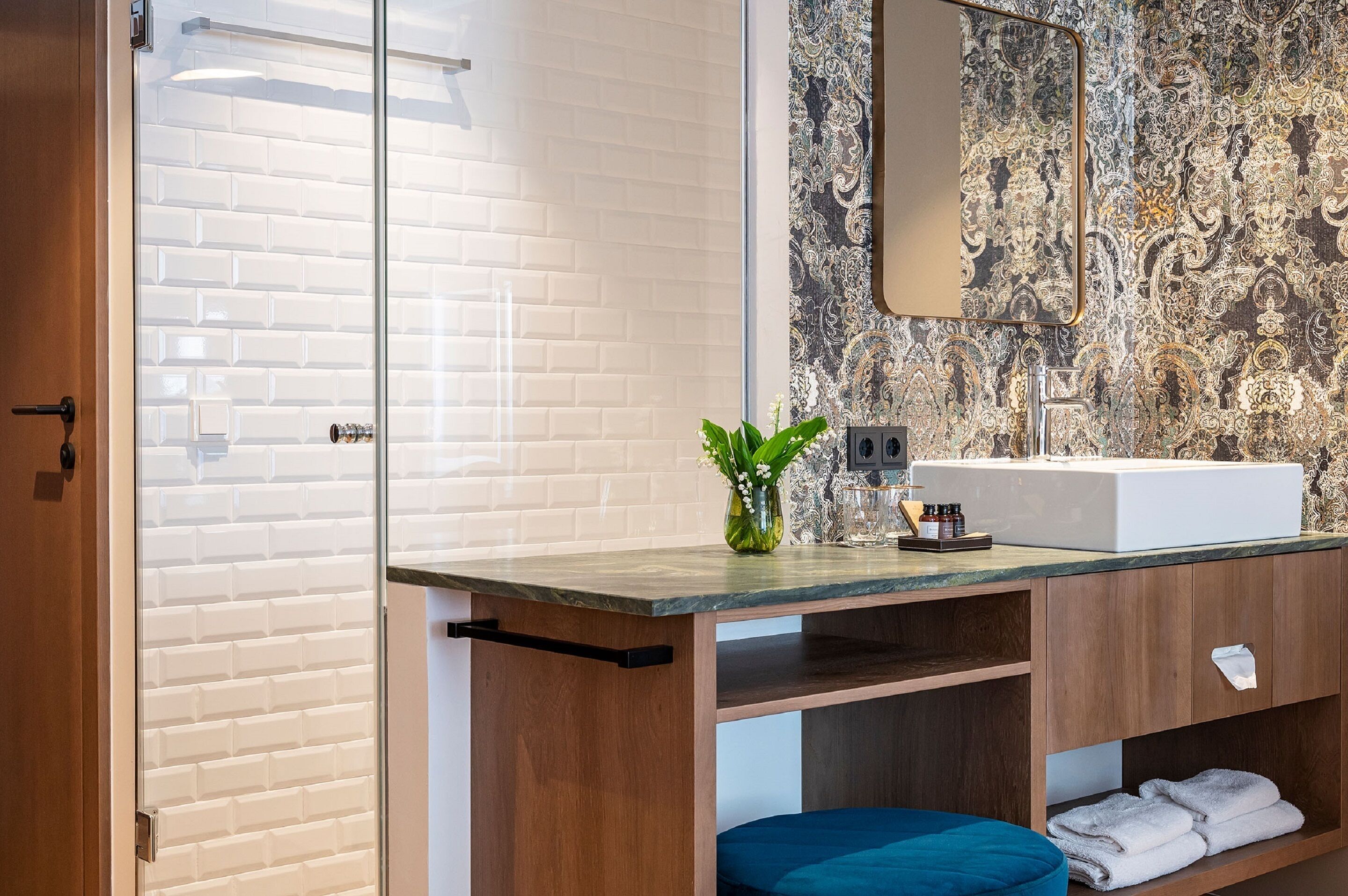 A modern bathroom with a white subway tile shower, a marble countertop, a sink with a mirror, and a patterned wall.